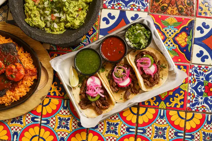 Tacos con salsas y guacamole sobre una mesa de azulejos de colores